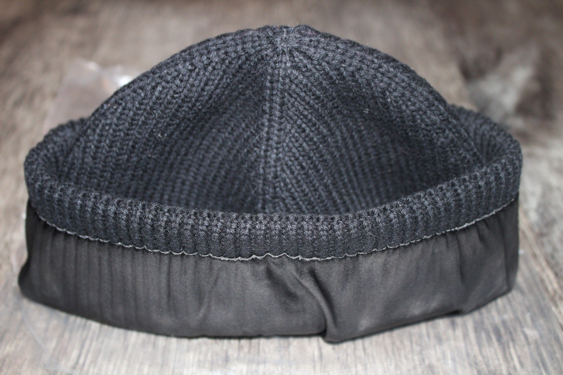 Black knitted beanie with black sating lining on a wooden surface